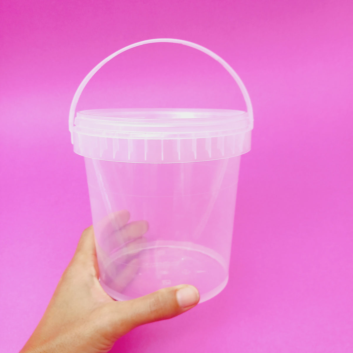 Secchiello trasparente con coperchio su sfondo rosa, retto da una mano