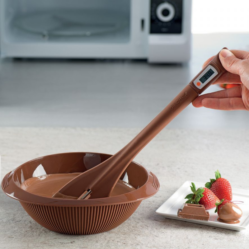 Mano che regge un termometro per cioccolato dentro una vaschetta in cui sta sciogliendo cioccolato 