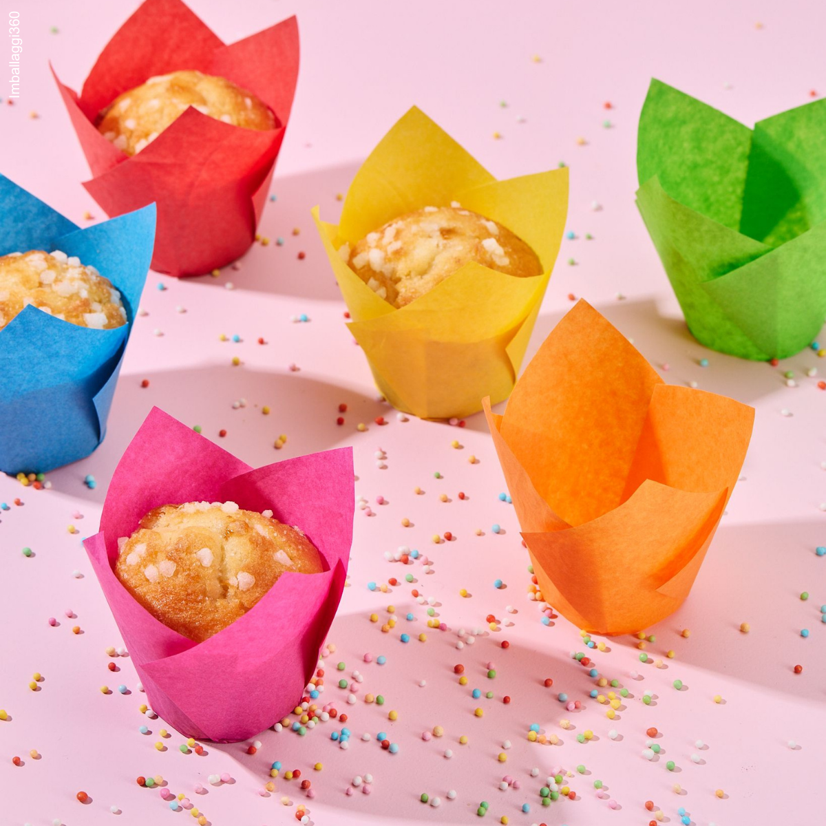 Pirottini colorati, alcuni pieni di dolci e due vuoti. Tutti su tavola rosa con zuccherini colorati sparsi 