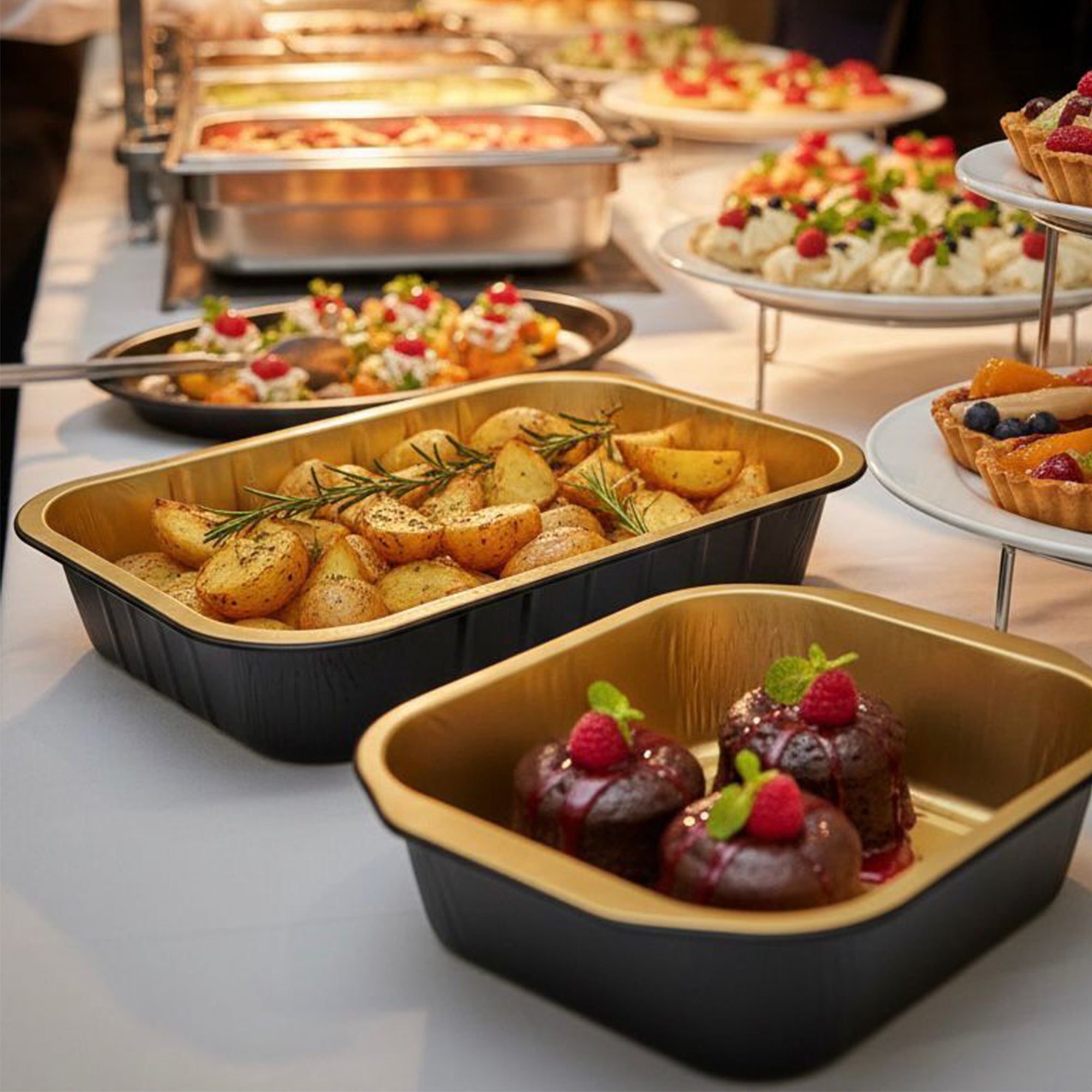 Vaschette in alluminio nere con interno dorato, piene di cibo, sul tavolo di un catering 