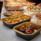 Vaschette in alluminio nere con interno dorato, piene di cibo, sul tavolo di un catering 