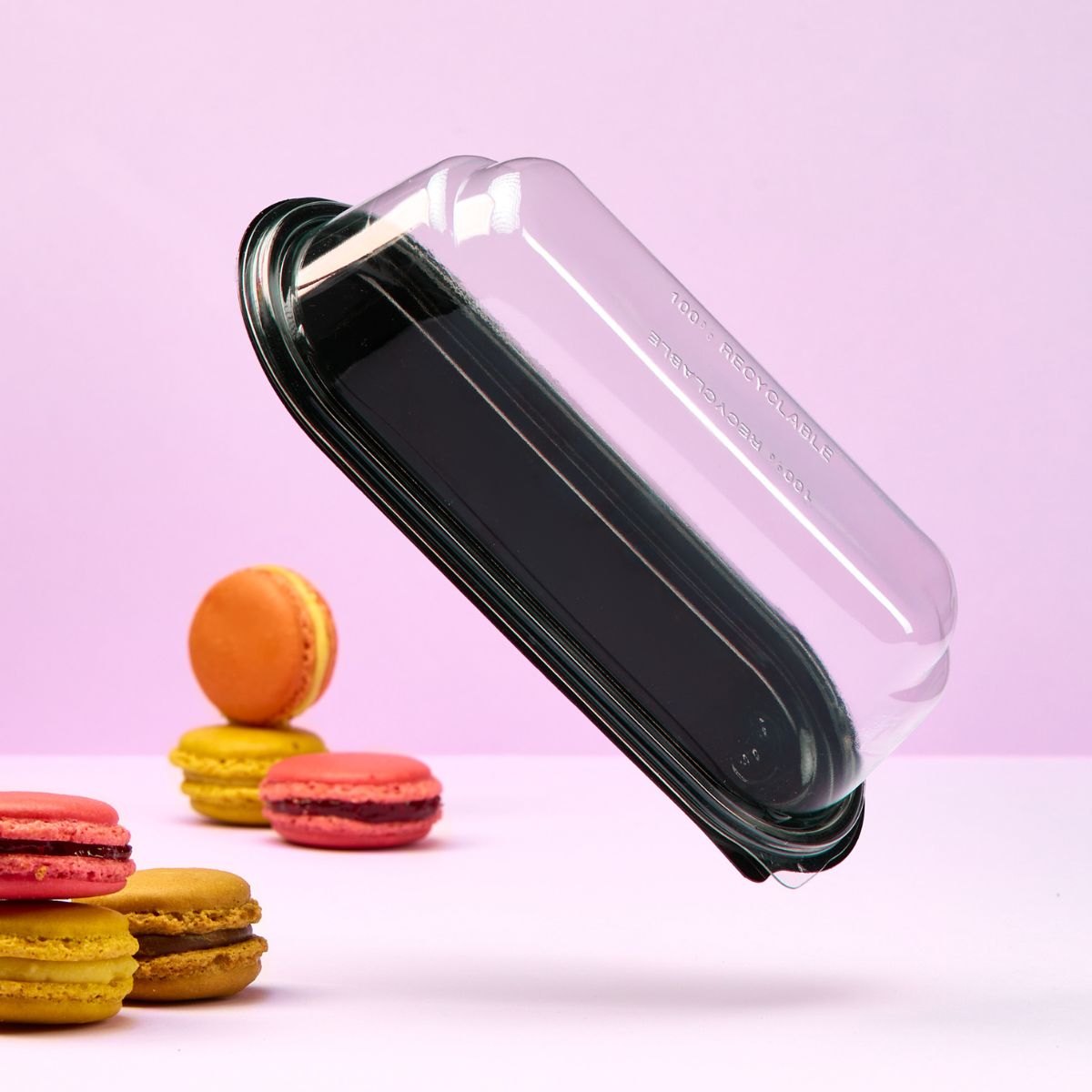 Vaschetta per monoporzioni, base nera coperchio trasparente, vuota, e macarons sparsi su sfondo rosa