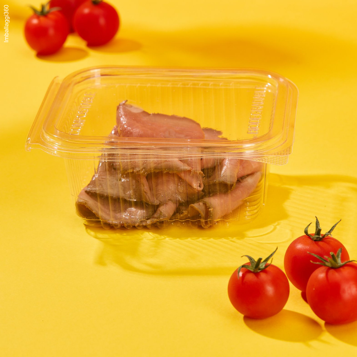 Vaschette trasparenti per gastronomia, mostrate chiuse e piene di cibo una sopra l'altra . Pomodorini sparsi tutto su sfondo giallo - dettaglio