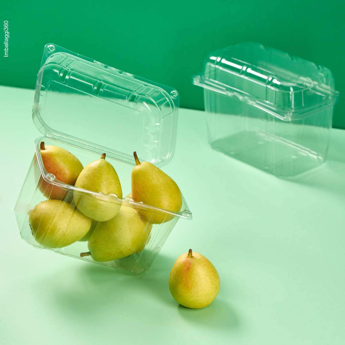 Vaschetta trasparente per frutta e verdura, ripiena di pere ed una vuota chiusa, su sfondo verde