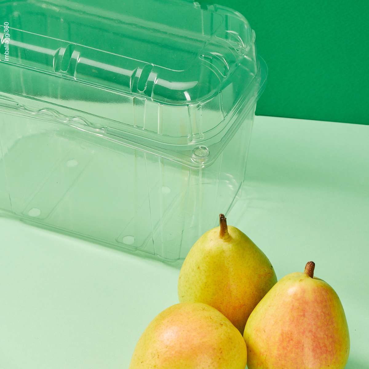 Vaschetta trasparente per frutta e verdura, vuota, dettaglio , su sfondo verde con pere