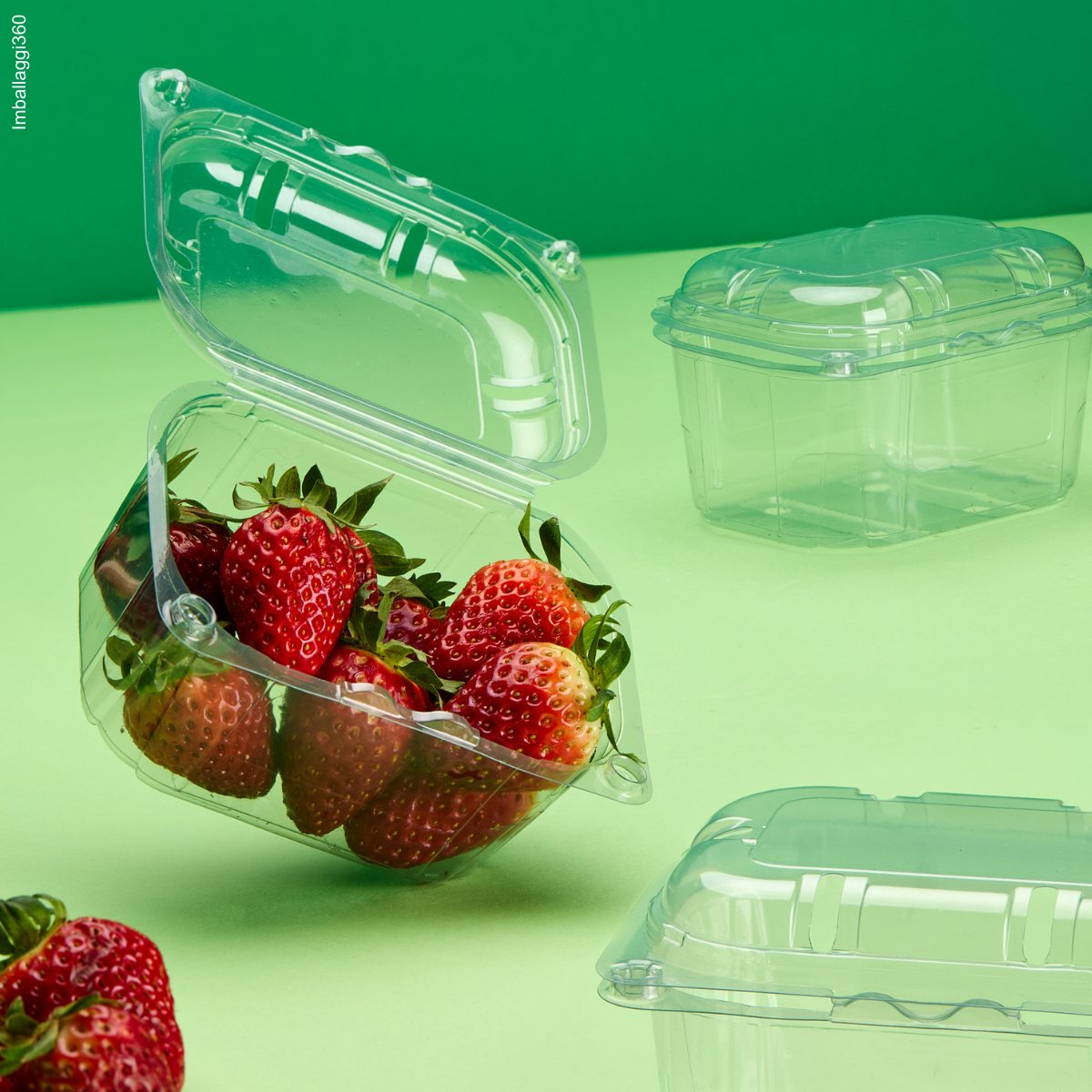 Vaschetta per frutta, su sfondo verde. Mostrata una piena di fragole, aperta e due chiuse vuote