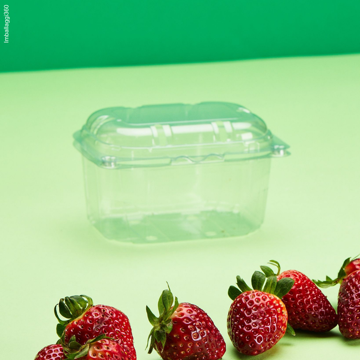 Vaschetta per frutta, su sfondo verde. Mostrata chiusa e vuota con fragole di fronte