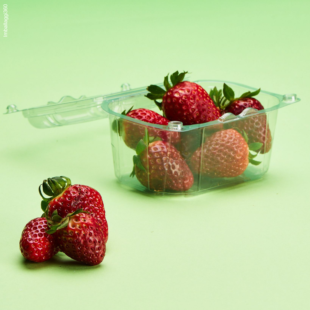 Vaschetta per frutta, su sfondo verde. Mostrata una piena di fragole, aperta e due fragole di fronte