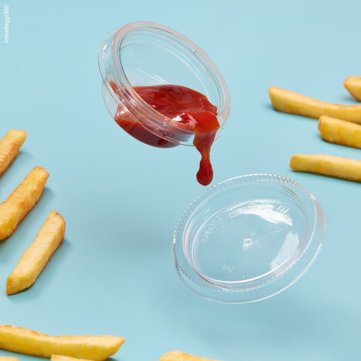 vaschetta di plastica per salsa mostrata piena di ketchup che sta cadendo sul suo tappo e la salsa fuoriesce, patatine intorno su uno sfondo azzurro