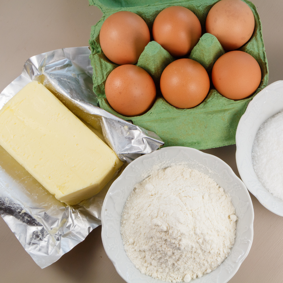 Visione dall'alto di tavola con farina, burro, portauova verde aperto con uova dentro