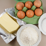 Visione dall'alto di tavola con farina, burro, portauova verde aperto con uova dentro