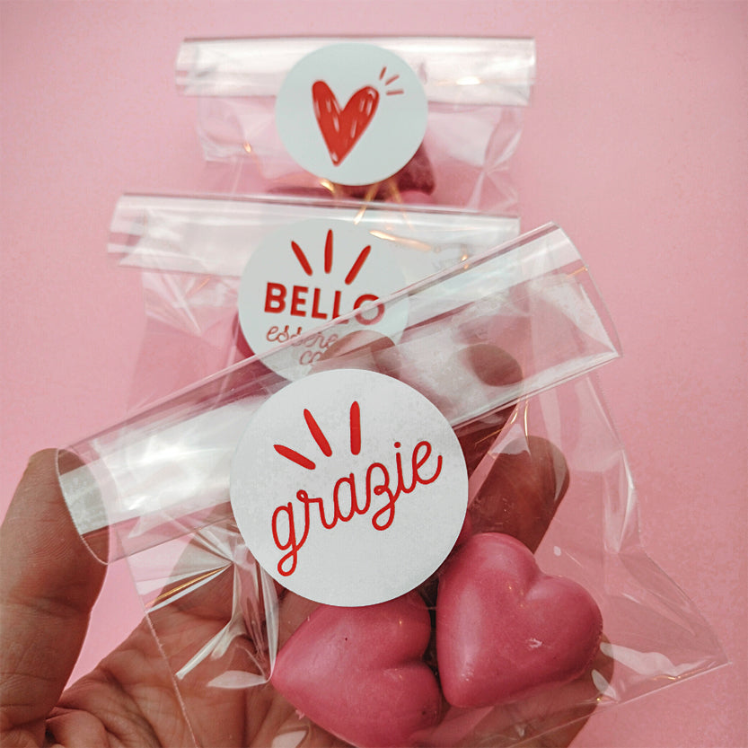 Bustine trasparenti piene di biscotti a forma di cuore rosa chiuse con etichetta tonda con scritte diverse