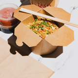 Contenitore cibo asporto aperto, di cartoncino, pieno di cibo con bacchette sopra su una tavola