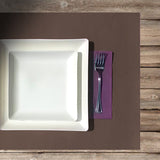 Apparecchiatura con tovaglietta americana marrone, tovagliolo di carta viola e due piatti in polpa di cellulosa quadrati uno sopra l'altro 