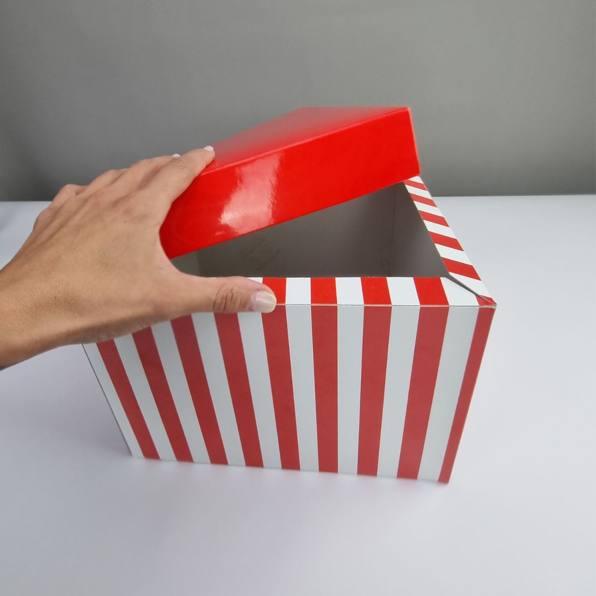 mano che apre scatola a righe verticali bianco e rosse e coperchio rosso 
