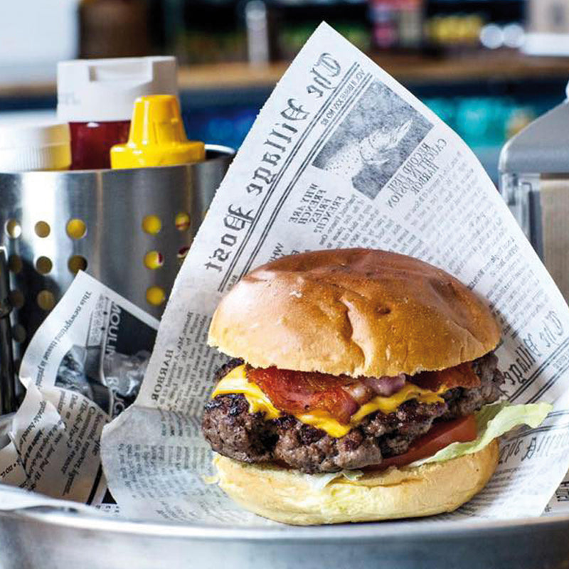 Hamburger nella sua carta antigrasso bianca con fantasia giornale su un piatto in un fast food