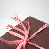 Pacco incartato con carta paglia marrone e nastro di  rafia rosa