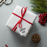 Pacco avvolto da carta bianca e fiocco rosso con cartellino open me 