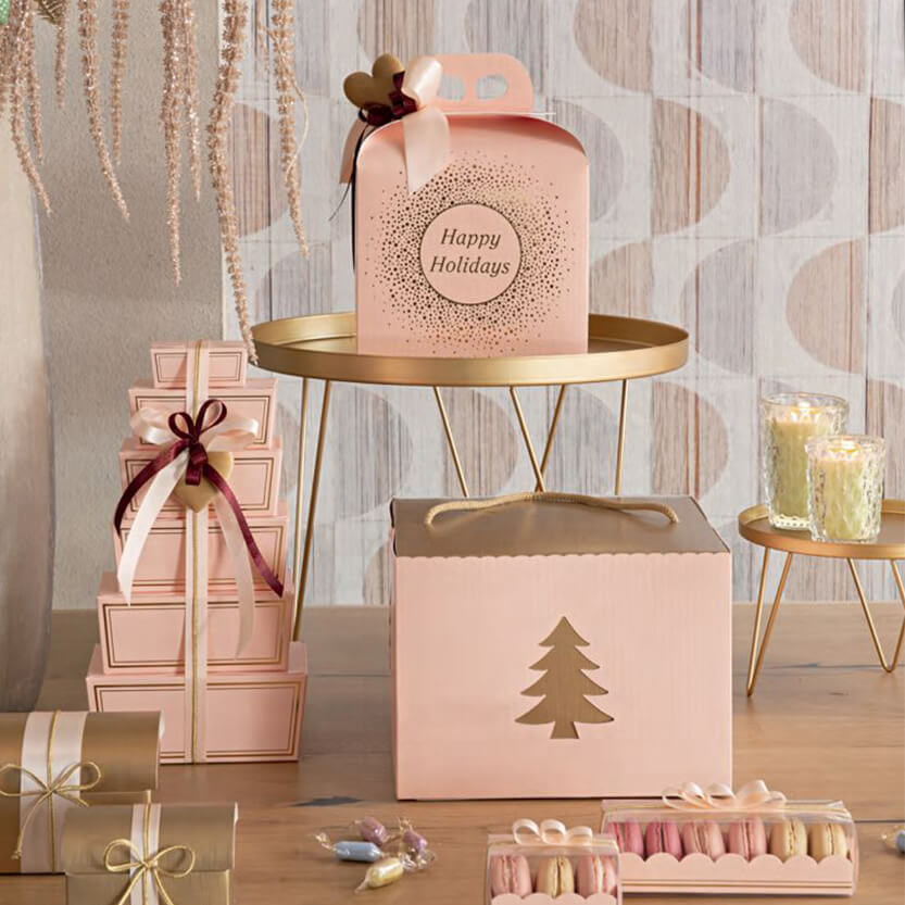 Confezioni per paste e panettoni color rosa su tavolino tra elementi della festa 