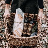 Ragazza che tine cestodi vimini quadrato con dentro due bottiglie di vino rosso e del pane avvolto nella carta 