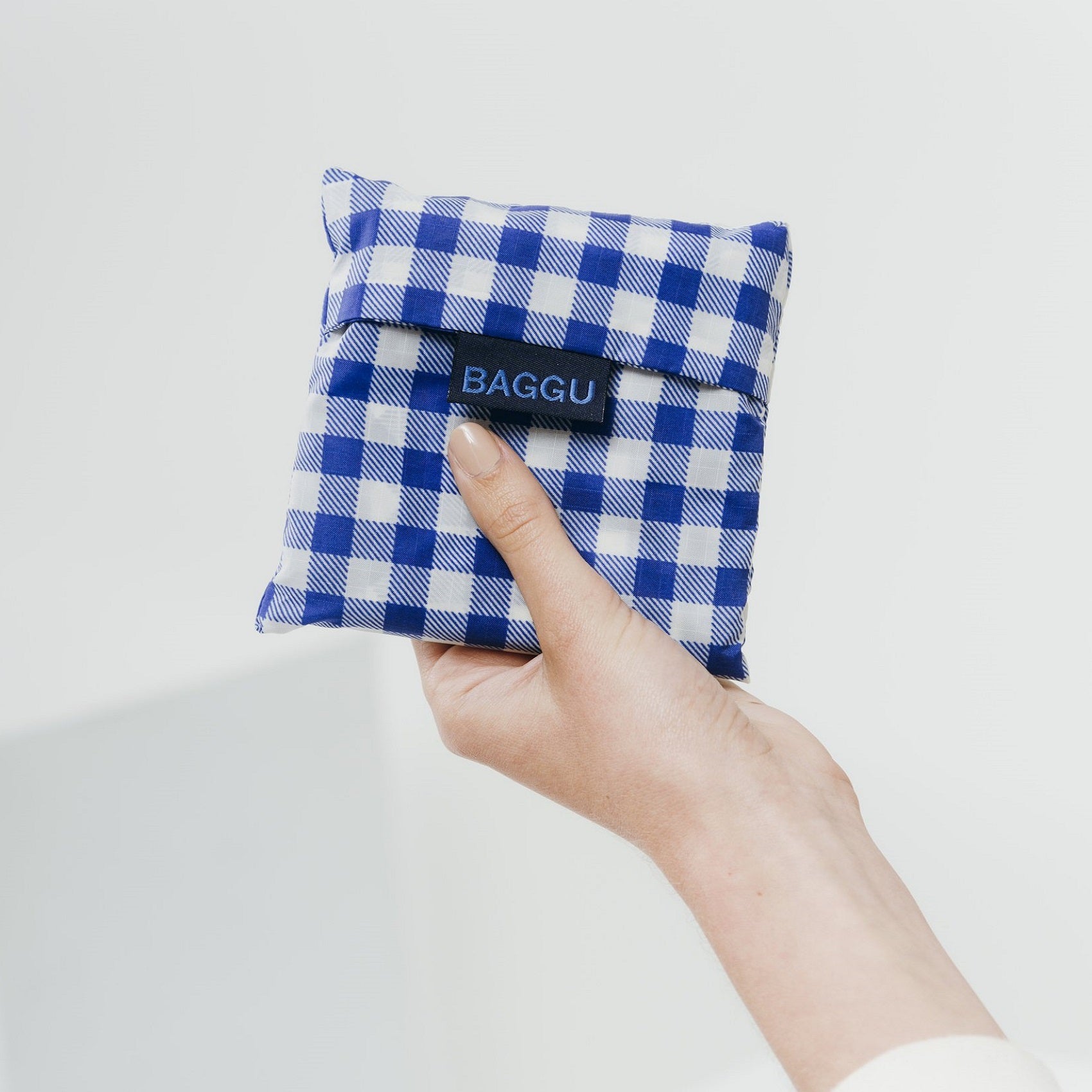 Mano che tiene busta a quadri bianchi e blu contenente shopper riutilizzabile 