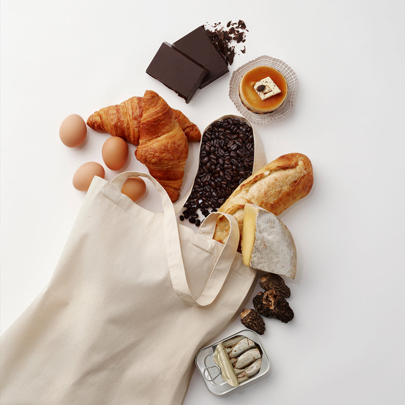 Shopper di tela bianca dalla quale escono prodotti da fono come pane e uova e caffe 