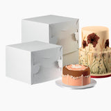 Scatole bianche quadrate per torte alte, due diverse misure, vicino a due torte 