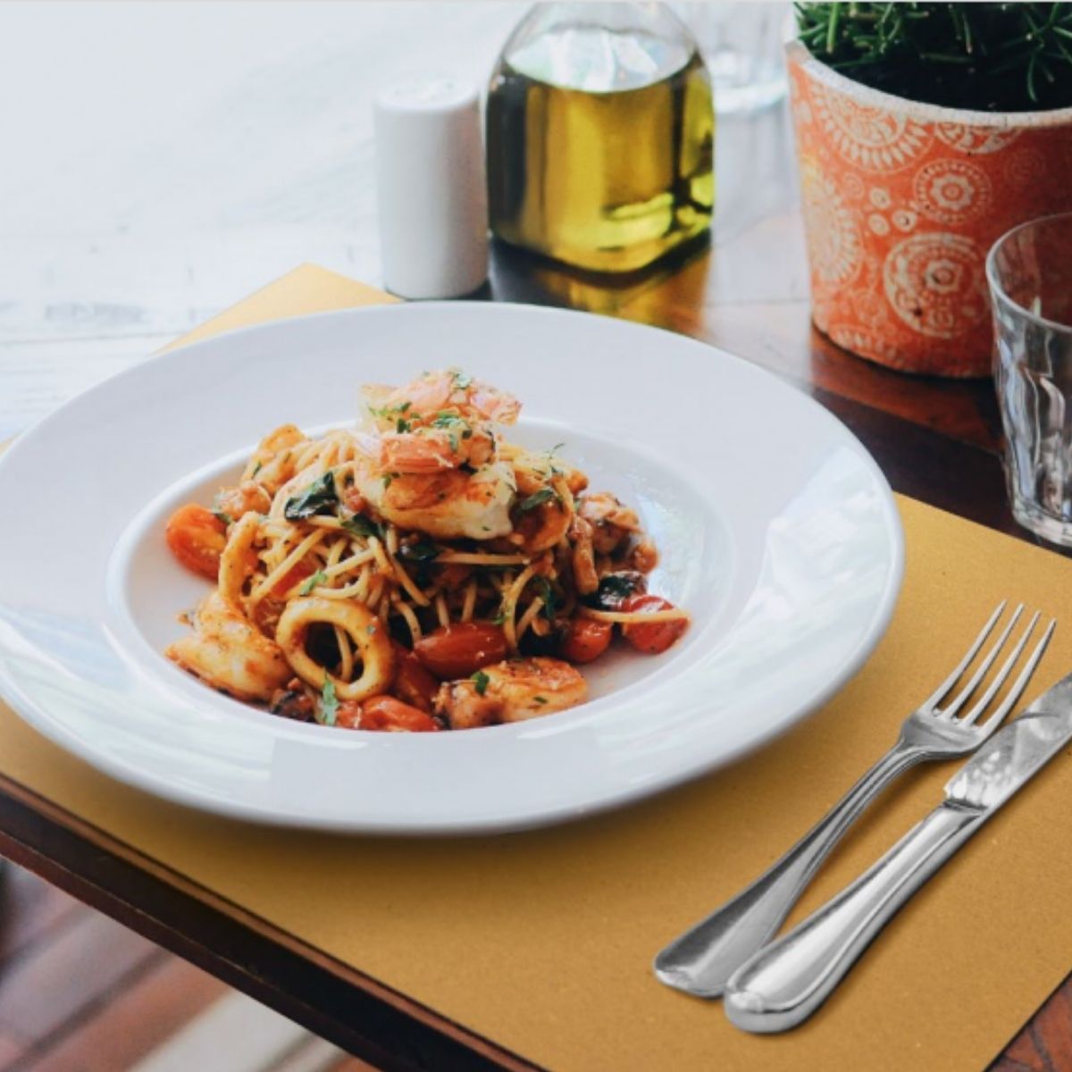 Piatto con un primo di pesce su tovaglietta carta paglia su tavolino 