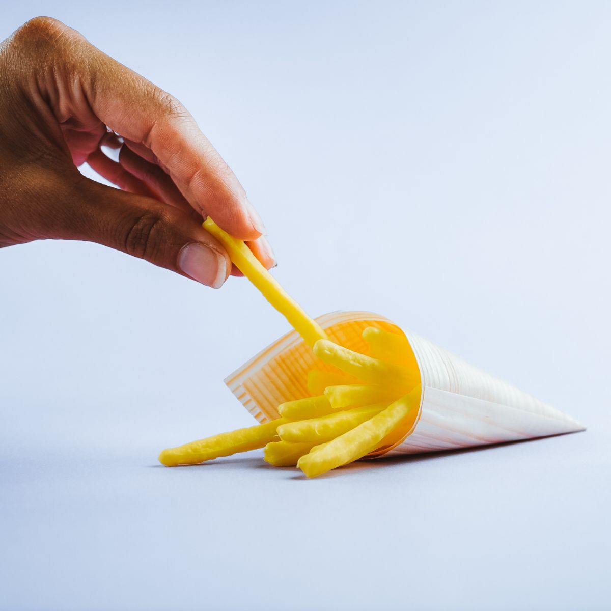 Mano che prende una patatina fritta da un cono di carta pieno di patatine 