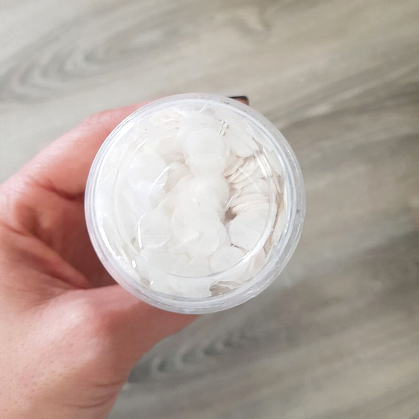 Mano che tiene vasetto di plastica trasparente con coperchio pieno di mandorle bianche tagliate a fette 