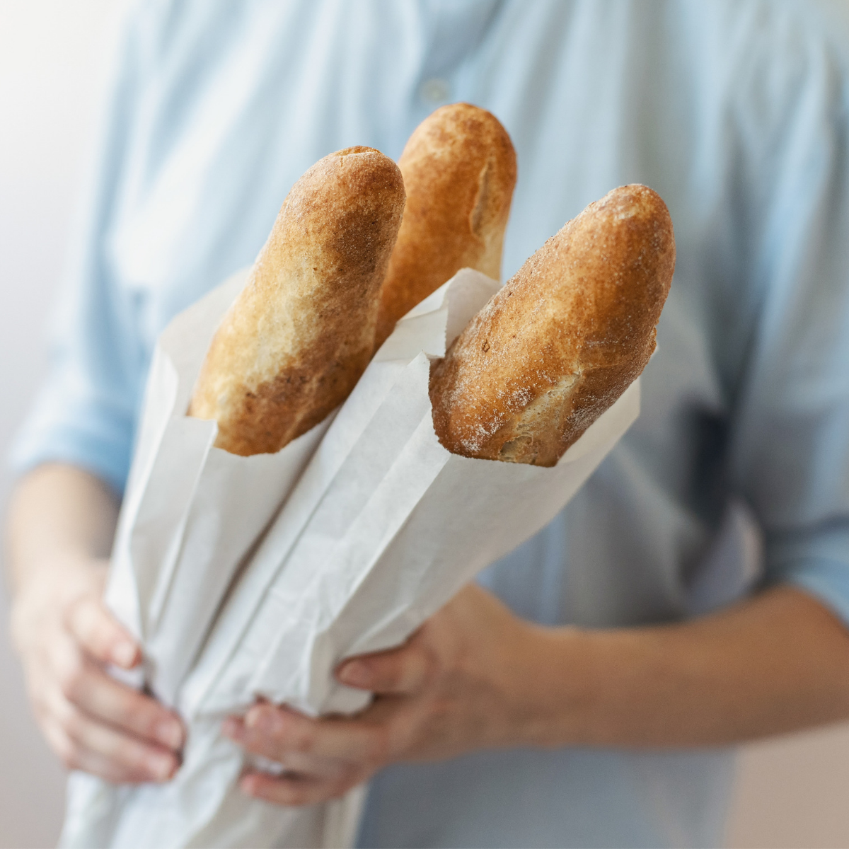 Mani che reggono tre sacchetti di carta bianca con pane dentro