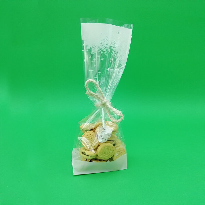 Sacchetto di plastica trasparente con fantasie bianche neve pieno di biscotti e legato con uno spago 