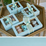 Tavolino con sopra scatole azzurre con finestra, di diverse dimensioni, infiocchettati e pieni di confetti