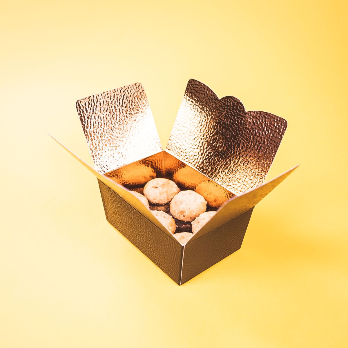 Scatola di carta metallizzata oro, aperta piena di baci di dama 